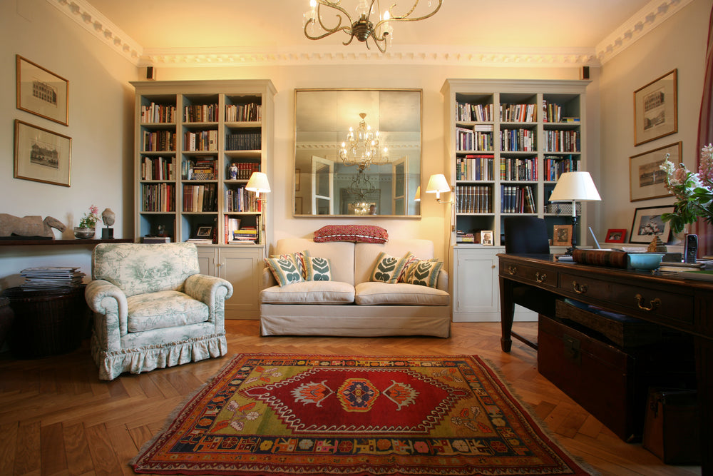Cozy home library with built-in bookshelves, patterned area rug, vintage armchair, neutral sofa, and elegant chandelier — styled reading room inspiration.