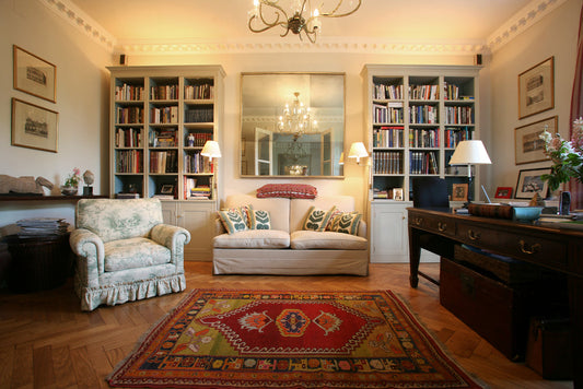Cozy home library with built-in bookshelves, patterned area rug, vintage armchair, neutral sofa, and elegant chandelier — styled reading room inspiration.