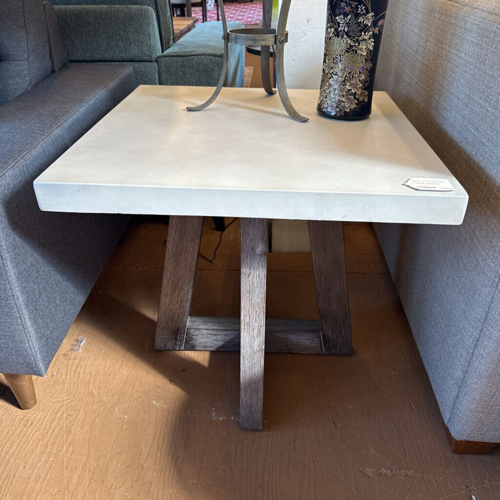 Small table with a concrete top and wooden legs in a room with gray couches.