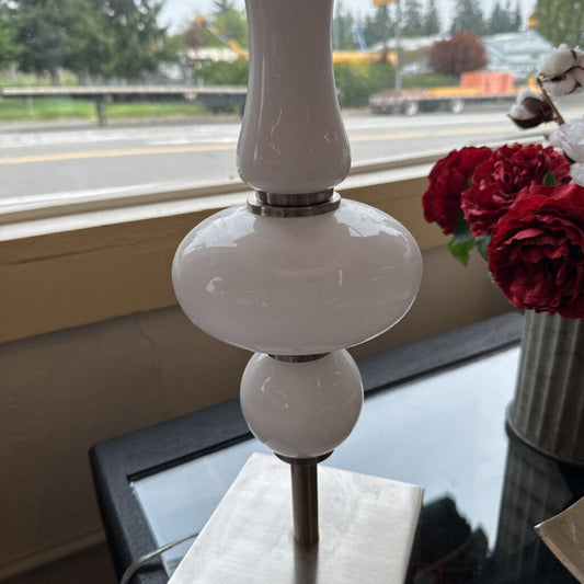 White lamp with decorative design on a table near a window with a view of a street.