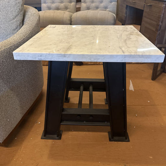 Table with marble-like top and black metal legs on a brown floor.