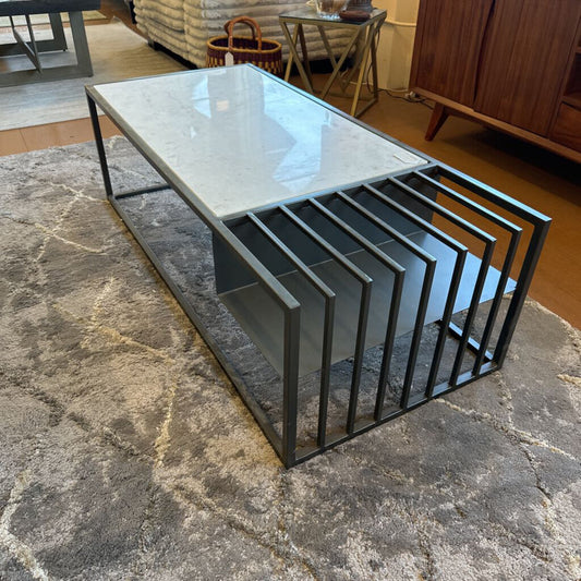 Modern coffee table with glass top and metal frame on a textured floor.