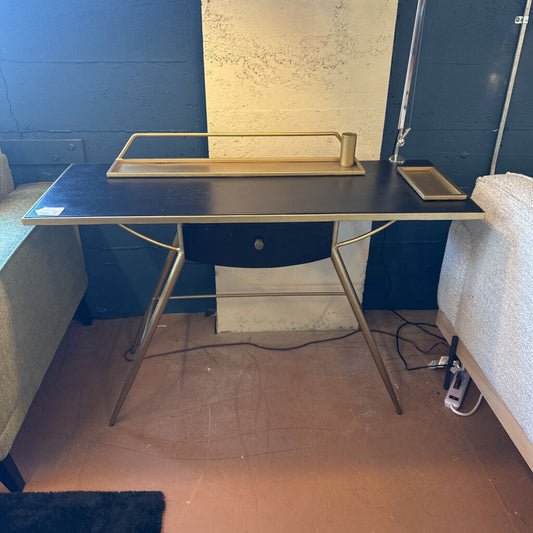 Black desk with gold legs in a room with blue walls and a whiteboard.