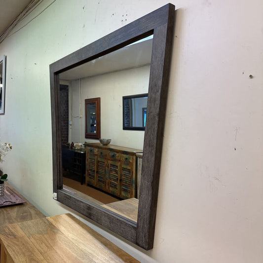 Wooden-framed mirror on a wall with a room reflection