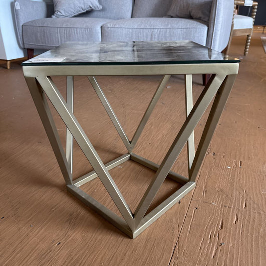 Glass top side table with gold geometric base on a wooden floor