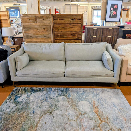 Light gray sofa in a room with wooden furniture and a patterned rug.