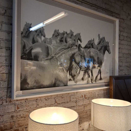 Framed artwork of horses running on a brick wall with two lamps below.