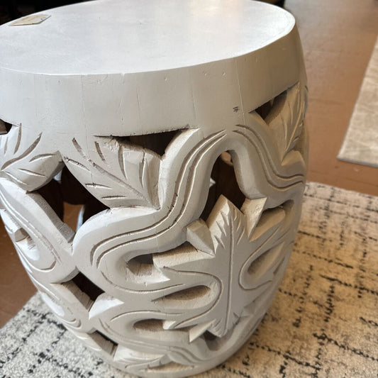Decorative white stool with leaf patterns on a textured surface