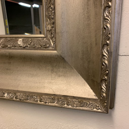 Decorative silver mirror with intricate designs on a plain background