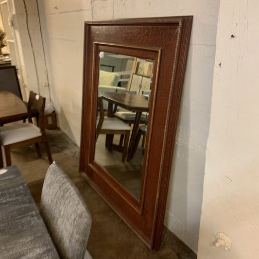 Wooden framed mirror leaning against a wall with a dining room reflection.