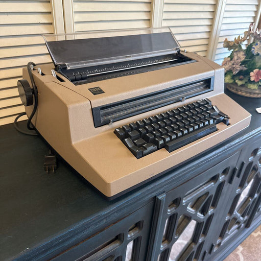 Beige typewriter on a dark surface with a window and decorative item in the background