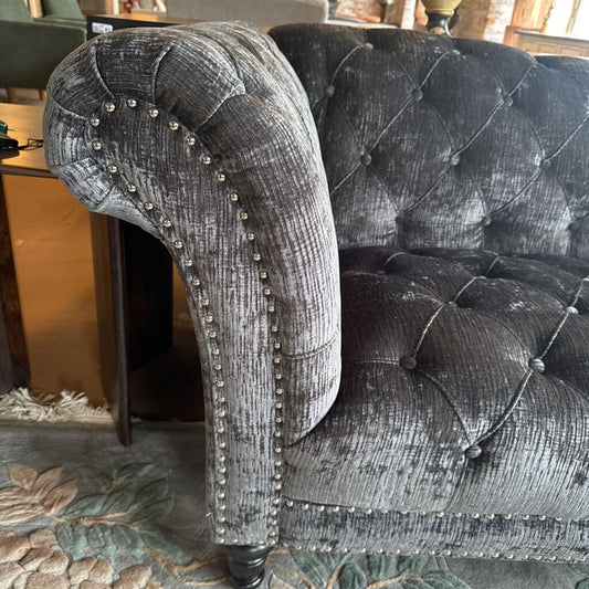 Gray tufted armchair with decorative nailhead trim on a patterned rug.
