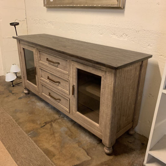 Wooden sideboard with drawers and glass panels in a room with a concrete floor.