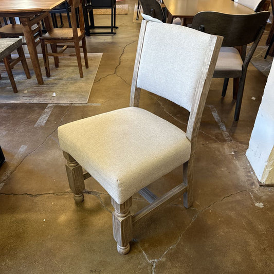 Dining chair with beige cushion on a concrete floor in a room with tables and chairs.