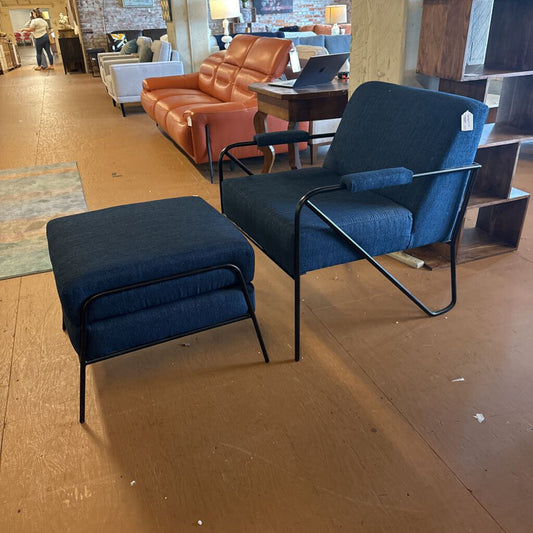 Blue chair and ottoman on a wooden floor with a brown couch in the background.