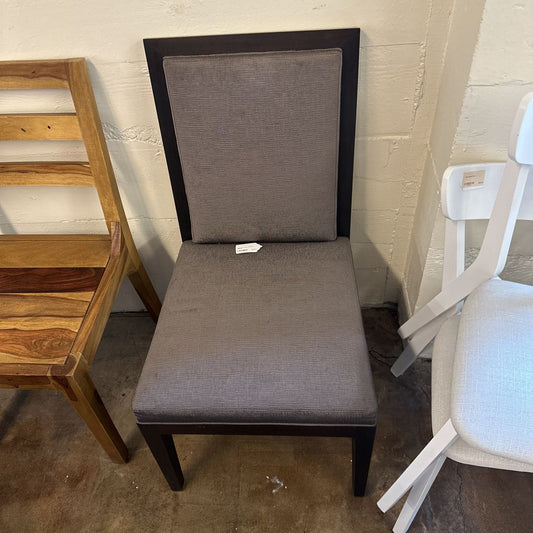 Gray upholstered chair with a wooden frame against a white wall.