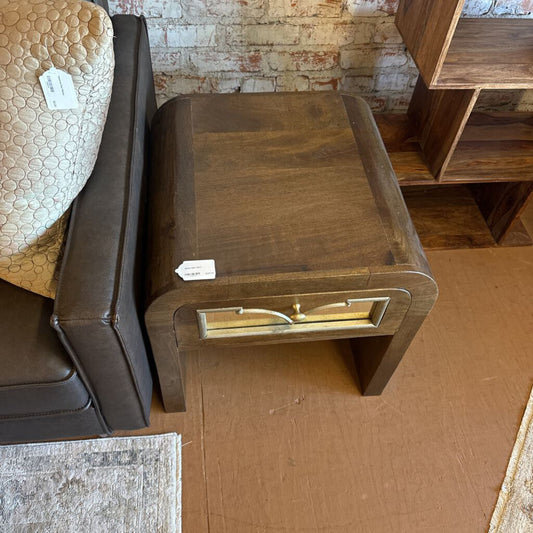 Wooden side table with a gold handle in a room with furniture and a brick wall.
