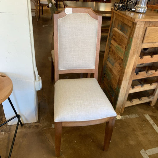 Wooden chair with beige cushioned seat and backrest in a warehouse setting.