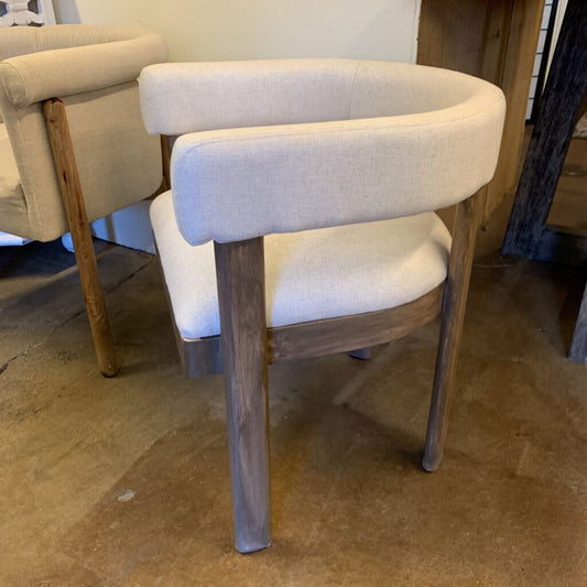 Chair with wooden legs and beige cushioned seat and backrest on a concrete floor.