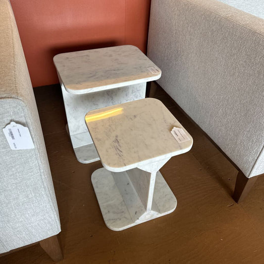 Two small tables with beige tops and white bases on a wooden floor.