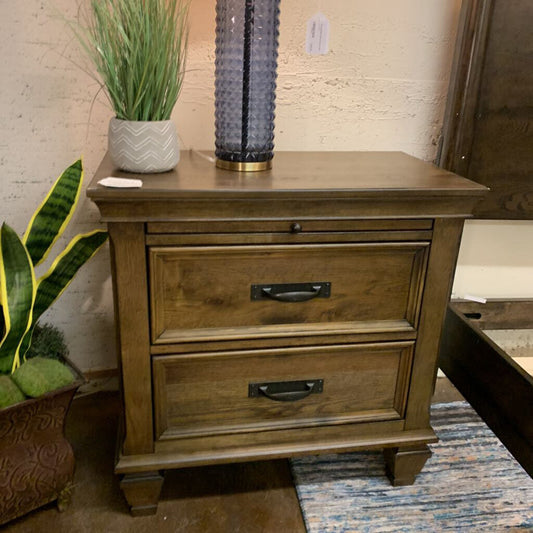 Wooden nightstand with two drawers, a plant, and a decorative item on top in a room setting.