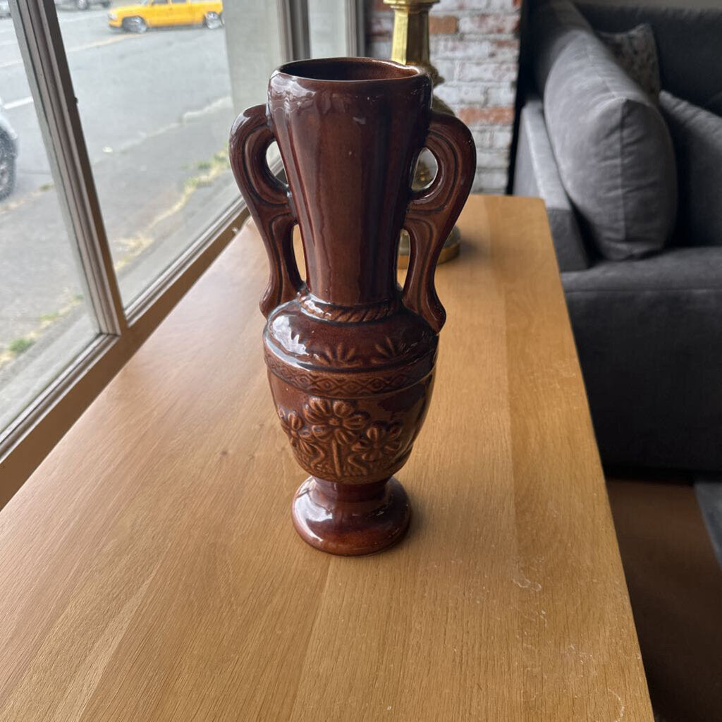 Brown decorative vase on a wooden surface with a window and sofa in the background