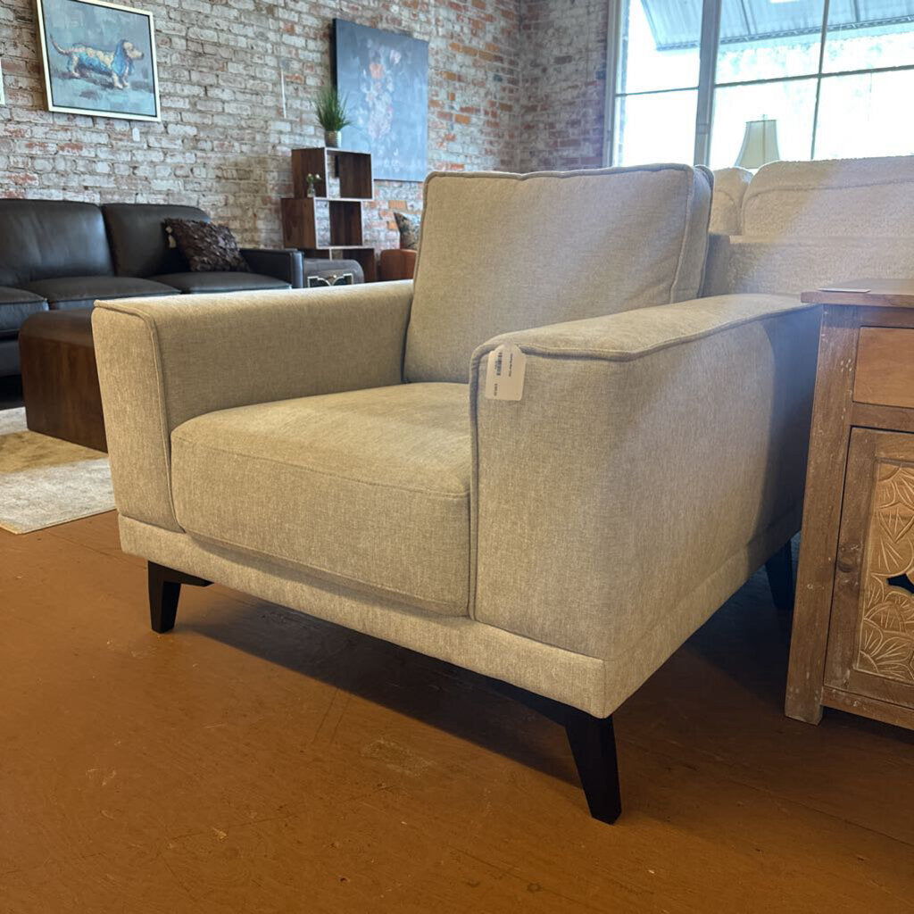 Beige armchair in a room with a brick wall and large windows.