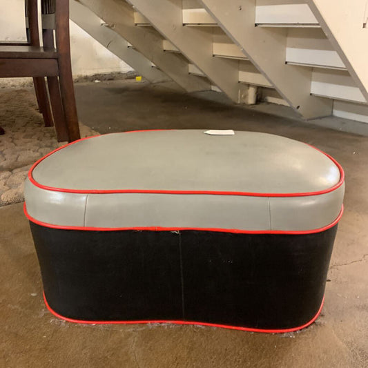 Oval-shaped ottoman with gray top and black base on a carpeted floor.