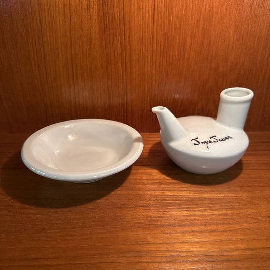 Two white ceramic items, a bowl and a ladle, on a wooden surface with a wooden background.