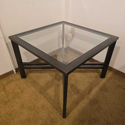 Square glass table with black frame on a carpeted floor against a white wall