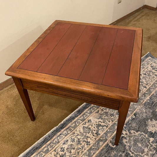 a small square wooden end table with one drawer and a wooden inlay top, in a showroom setting