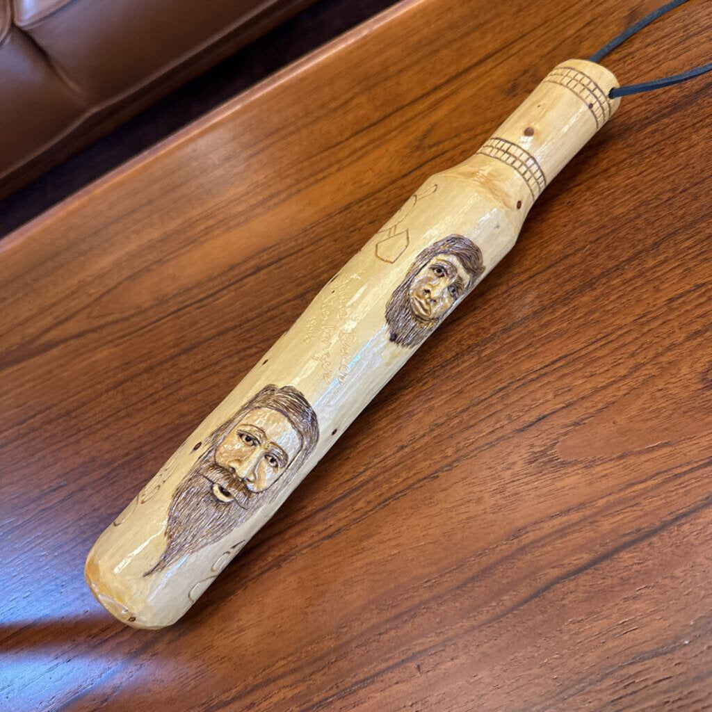 Wooden tool with engraved faces on a wooden surface