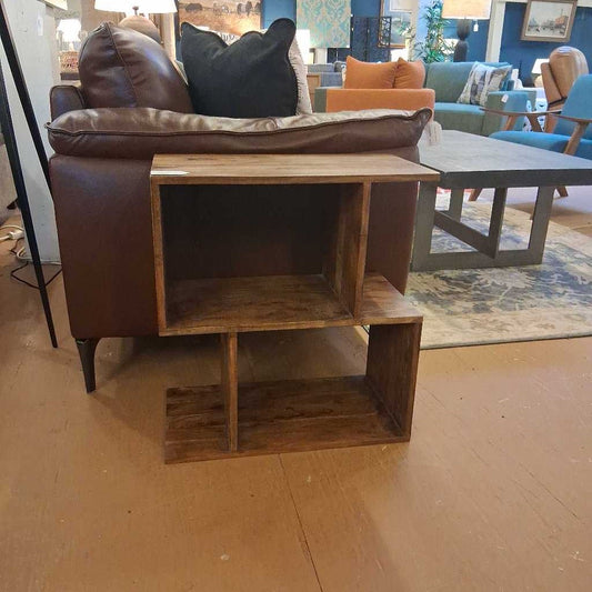 Wooden side table in front of a brown sofa with cushions in a living room setting.