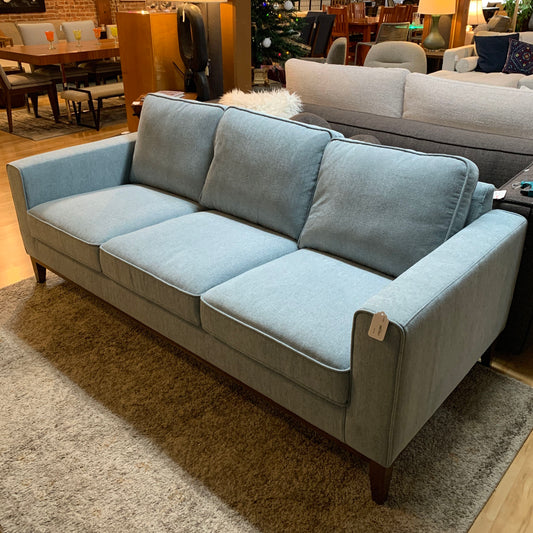 Light blue sofa in a showroom setting with other furniture and decor items.