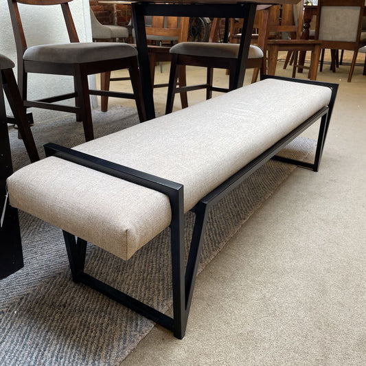 A long, narrow bench with cream-colored textured upholstery and a modern black metal frame that wraps over the ends of the seat.