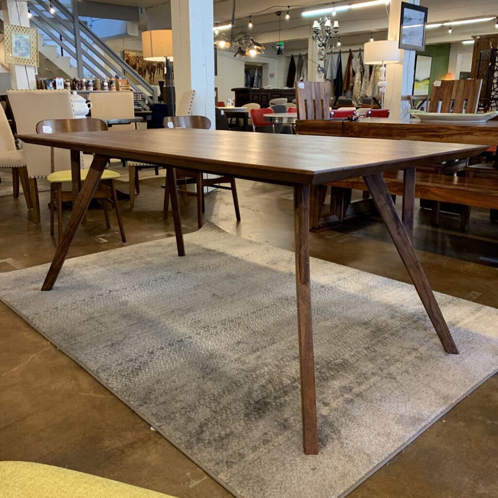 Wooden dining table in a showroom setting with chairs and decor.