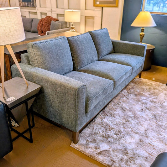 Gray sofa in a living room setting with lamps and a rug.