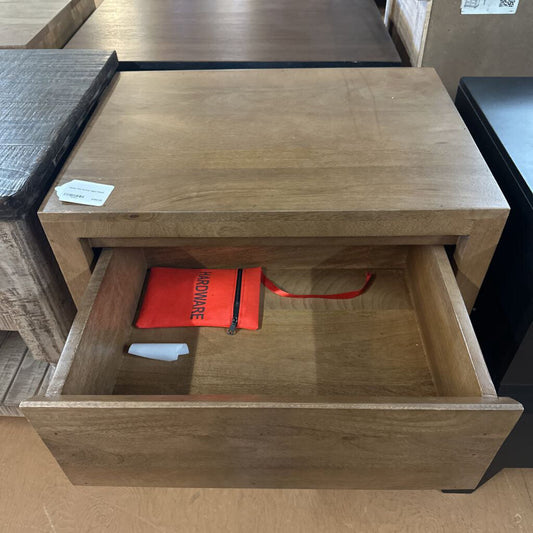 Wooden side table with an open drawer containing a red bag, on a wooden floor.