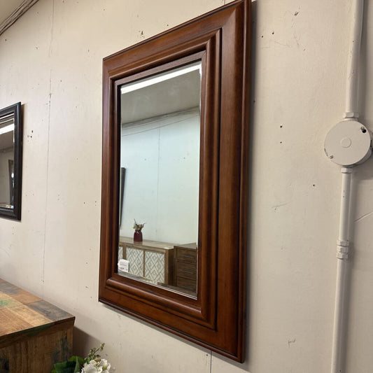 Wooden-framed mirror on a textured wall with visible pipes.