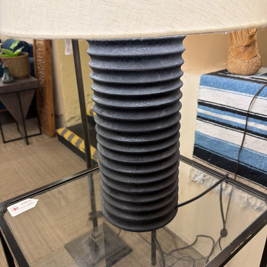 Table lamp with ribbed black base and beige lampshade on a glass table.