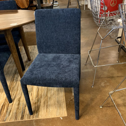 Blue chair on a wooden floor with other chairs and a shopping cart in the background.