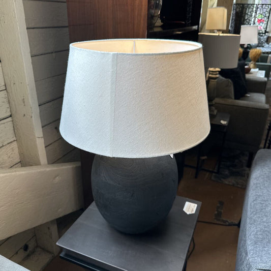 Table lamp with a gray base and white shade on a table in a room setting.