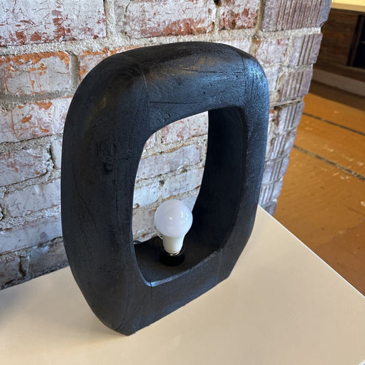 Black abstract sculpture with a light bulb inside against a brick wall.