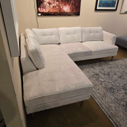 Gray sectional sofa in a living room setting with a rug and wall art.