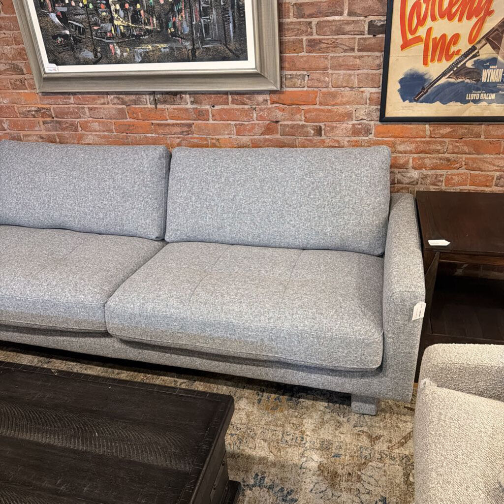 Gray sofa in a room with a brick wall and framed pictures.