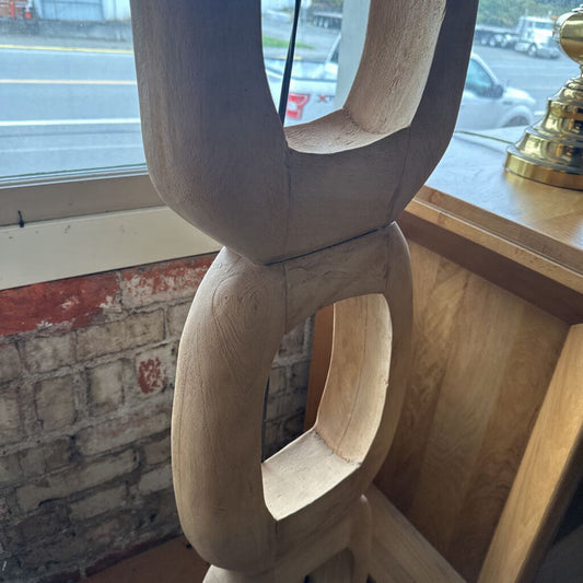 Wooden sculpture with circular design in a room with a window and brick wall.