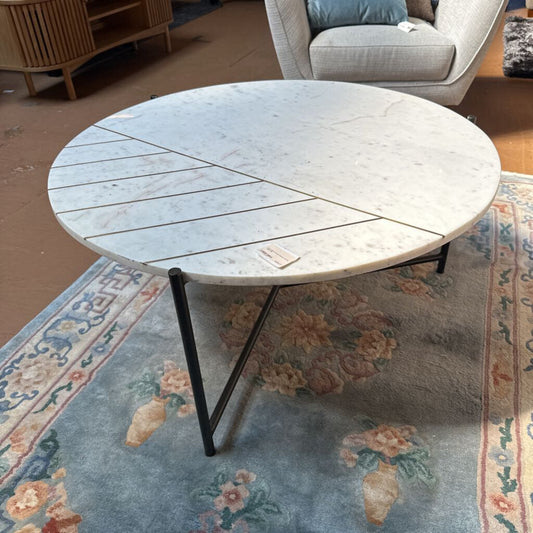 Round coffee table with a white marble-like top and black metal legs in a living room setting.