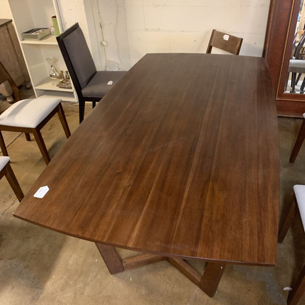 Wooden dining table in a showroom setting with chairs around it.