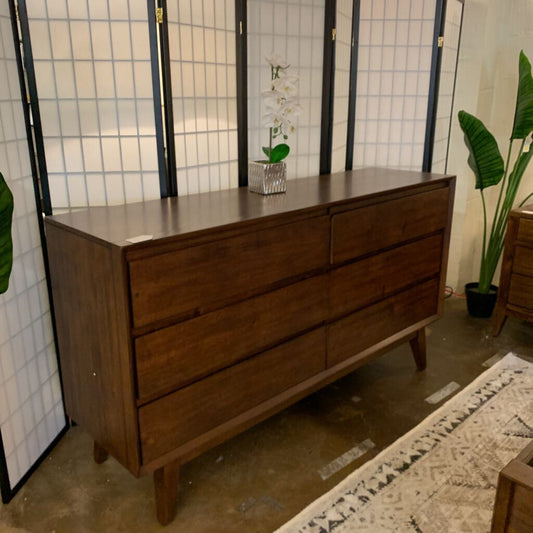 Wooden dresser with four drawers in a room with plants and a rug.
