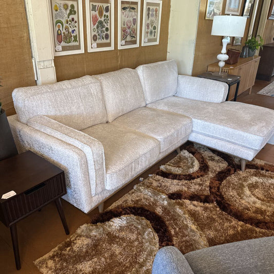 Beige sectional sofa in a living room setting with a patterned rug and framed artwork on the wall.
